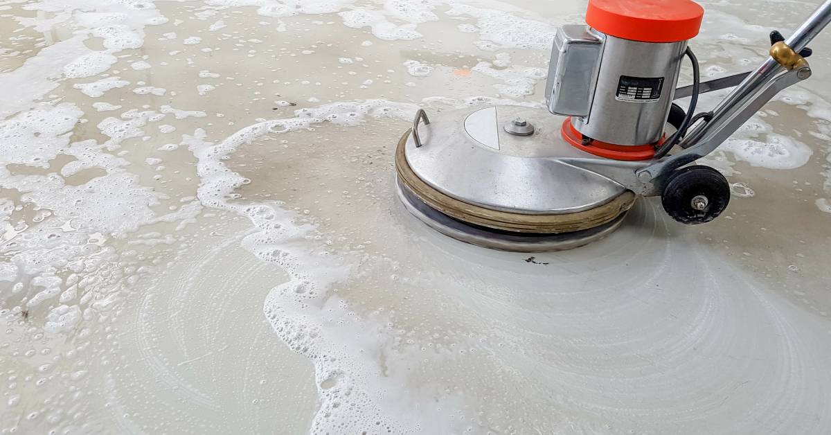 A scrubber machine cleaning the correctional facility’s floor. The polished concrete has patches of soap suds.